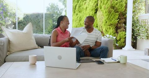 Couple discussing documents cheerfully at home with laptop and papers