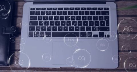 Overhead Silver Laptop Displaying Keyboard and Trackpad with Floating 6G Bubbles on Wooden Desk