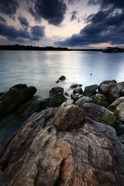 Dramatic cloudy sky and twilight hues create a serene atmosphere over rocky shoreline and calm sea. Ideal for backgrounds, travel blogs, or nature-themed projects, emphasizing tranquility and natural beauty.