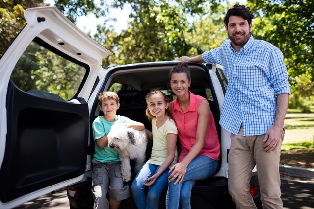 Portrait of happy family sitting in car trunk with their dog