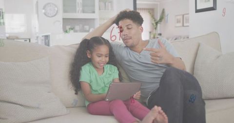 Father and daughter sharing tablet on couch, cozy home learning and bonding in living room