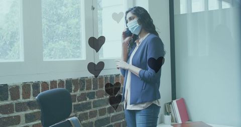 Businesswoman in Mask on Phone Call with Floating Hearts in Office