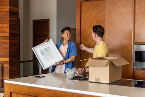 Two asian men unpacking and arranging framed artwork on modern kitchen island