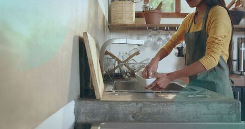 Washing dishes in rustic concrete kitchen with curved faucet and warm natural light