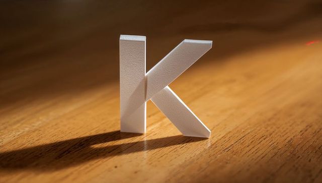 3d white letter 'k' on wooden desk under warm lighting