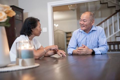 Mature asian couple sharing warm conversation at candlelit dining table, cozy home moment