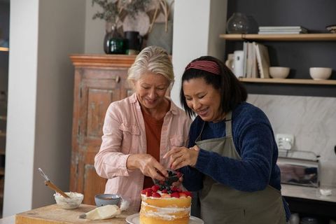 Two Women Decorating Naked Layer Cake with Fresh Berries in Cozy Kitchen
