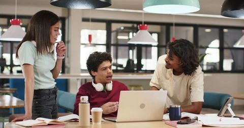 Diverse students collaborating in modern coworking space with laptop and notebooks