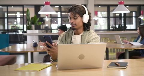African american man working on laptop and checking smartphone in modern coworking cafe