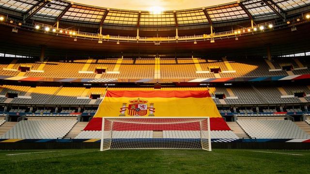 Spanish flag draping stadium lower stands with regulation goal on sunlit football pitch