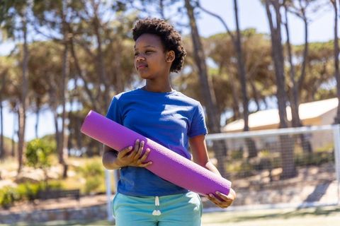 African american teen holding purple yoga mat on sunny soccer field boosting youth fitness