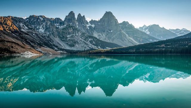 Reflecting jagged peaks mirroring in turquoise glacial lake with conifer treeline