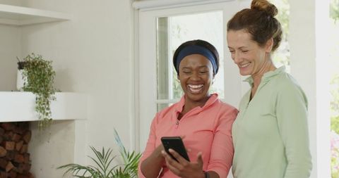Diverse Female Friends Laughing While Looking at Smartphone Indoors