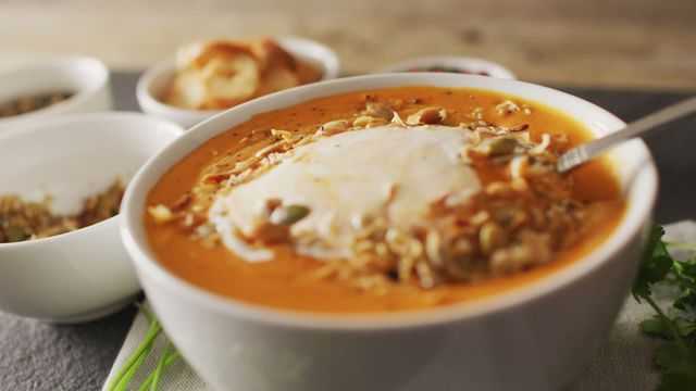 Deliciously presented bowl of creamy pumpkin soup topped with seeds and fresh herbs. Image captures home-cooked warmth and nutritionalful food. Perfect for illustrating healthy eating, autumn recipes, or culinary blogs showcasing vegetarian meal ideas. Great use in food-based social media or websites targeting nutritious recipes.