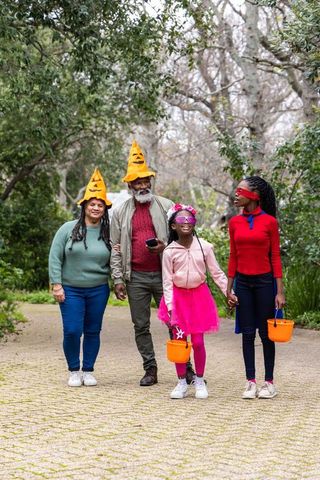 African american family walking in halloween costumes with orange trick-or-treat buckets