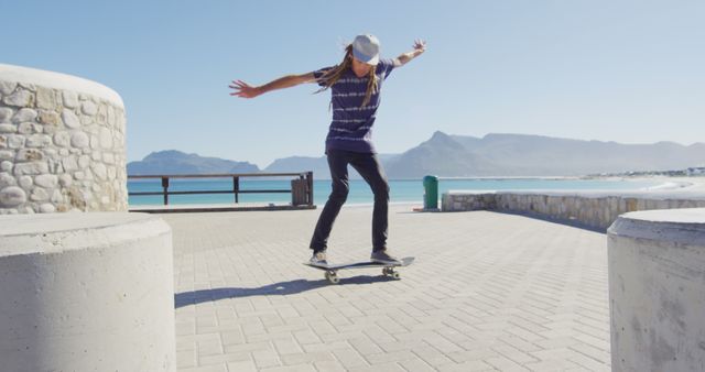 Young man skateboarding and practicing tricks by the seaside on a sunny day. Ideal for illustrating outdoor activities, youth culture, and adventure sports, especially related to coastal or beachside environments. Useful for blogs or advertisements promoting active lifestyles, sports equipment, or travel destinations.