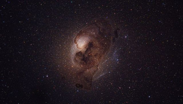 Glowing emission nebula revealing warm core and dark dust lanes in star field