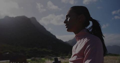 Backlit woman standing on mountain trail holding water bottle at sunrise hiking fitness
