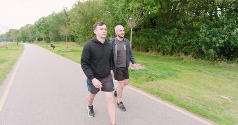 Two men walking outdoors on park path, embracing fitness and companionship