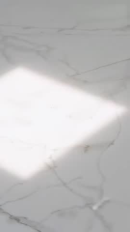 Vertical video of shifting sunlight sliding across polished white marble with soft veining