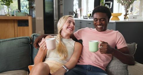 Smiling Diverse Couple Enjoying Coffee on Cozy Sofa in Modern Living Room