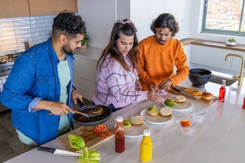 Friends preparing burgers at kitchen island, casual cooking together with toppings