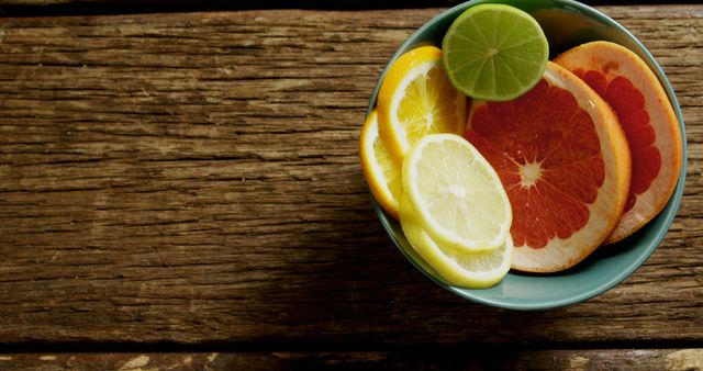 Citrus slices, including lemon, lime, and grapefruit, arranged in a blue bowl on a rustic wooden table. Ideal for use in articles about healthy eating, recipes, diet and nutrition, organic food, or refreshing summer drinks. Also suitable for backgrounds or textures in food and lifestyle content.