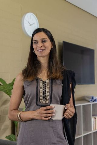 Indian woman standing holding mug in modern lounge wearing embroidered kurta