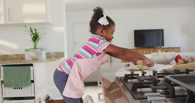 Little girl enthusiastically baking in bright modern kitchen using rolling pin and countertop. Great for ads relating to family activities, childhood, home life, teaching kids to cook, and modern kitchen designs.