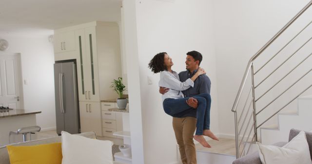 Happy romantic hispanic man carrying woman downstairs in living room. at home in isolation during quarantine lockdown.