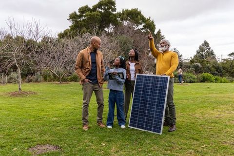 Multigenerational family exploring solar power while holding panel and tablet in park