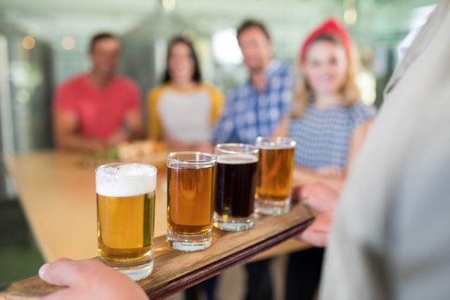Bartender presenting a flight of various beers to a group of friends at a bar. Ideal for use in articles or advertisements related to social gatherings, craft beer tasting events, pub promotions, and leisure activities.