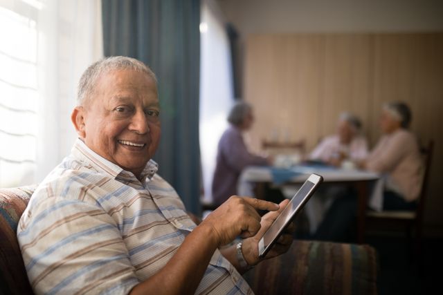 Portrait of smiling senior man using digital tablet while sitting on sofa with friends in background