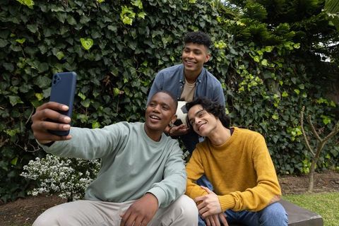 Teen friends taking backyard selfie while holding soccer ball and laughing together