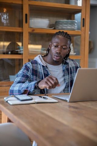 Focused Man Working at Home Desk Using Laptop and Notebook