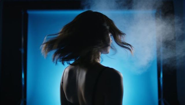 Backlit woman spinning hair against blue gradient backdrop with cinematic fog, rim light