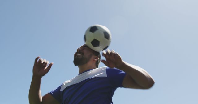 Young athlete demonstrates skill by heading soccer ball outdoors with clear blue sky in background. Ideal for use in advertisements promoting sports equipment, fitness programs, energy drinks, or team sports campaigns highlighting skill and teamwork.