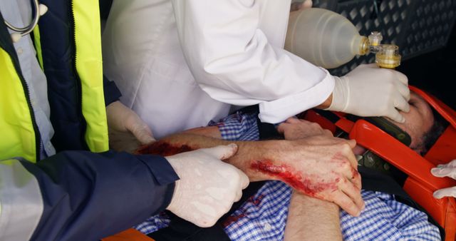Paramedics are giving emergency first aid to an injured man with a bloody arm inside an ambulance. This image can be used to highlight emergency medical services, training materials for first responders, healthcare articles, and accident prevention campaigns.