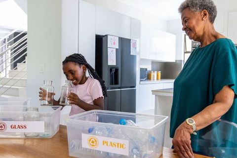 African grandmother and granddaughter sorting recycling in bright modern kitchen