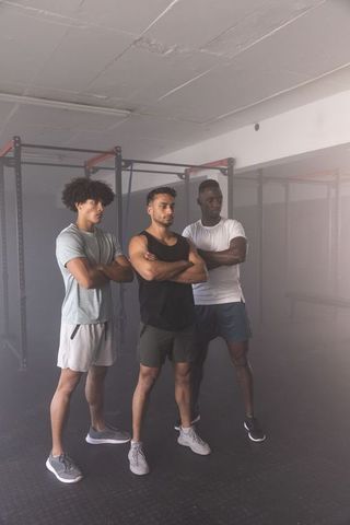 Diverse fitness trio posing with arms crossed in industrial gym conveying team strength