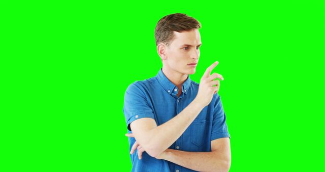 Young man in casual blue shirt, pointing with serious expression against green screen background. Ideal for illustrating concepts of decision making, direction, instruction, or offering ideas in presentations, advertisements, and educational materials. Green screen makes it easy to overlay different backgrounds or integrate into video projects.