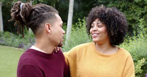 Smiling couple sitting in garden wearing mustard yellow and burgundy knit sweaters