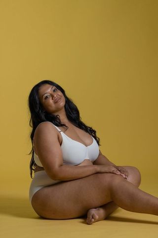 Curvy asian woman sitting in white underwear on mustard background, body positive portrait