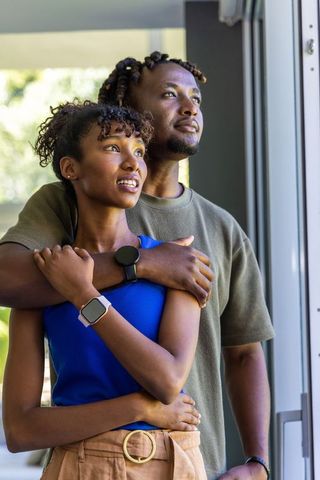African american couple embracing by sliding door wearing smartwatches in morning light