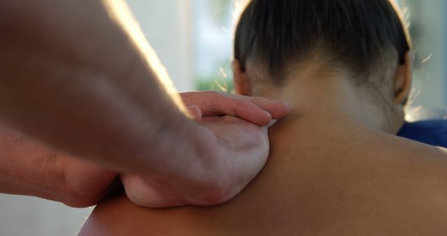A close-up view of a person receiving a therapeutic shoulder massage from a masseur, with copy space. Massage therapy is often sought for relaxation and relief from muscular tension or pain.