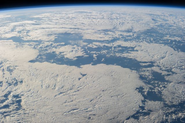 View of a cloud-covered part of Earth taken by an Expedition 40 crew member aboard the International Space Station in June 2014. This image captures the vast blanket of clouds covering the planet's surface with the faint glow of the horizon at the top. Ideal for educational materials, space exploration presentations, environmental studies, and astronomy enthusiasts.
