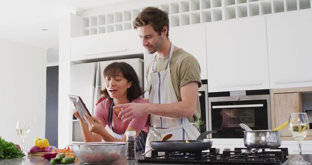 Image of happy diverse couple preparing meal together with tablet. Love, relationship and spending quality time together concept.