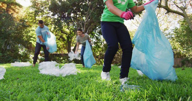 Three individuals participating in a community service activity, picking up trash in a park. They are using blue bags to collect plastic waste, showcasing an effort towards environmental conservation. Perfect for illustrating community engagement, environmental awareness, or volunteer work initiatives and promotional materials for eco-friendly activities.