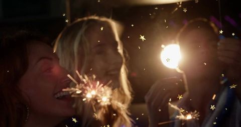 Friends celebrating with sparklers at night party, warm glow and confetti stars candid