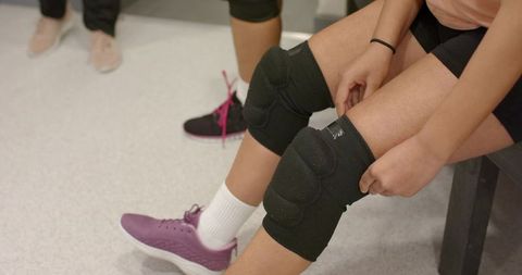 Female athletes preparing on bench adjusting black knee sleeves in locker room